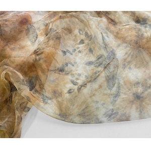 May include: A sheer fabric with a brown and gray leaf pattern. The fabric is translucent and has a soft, flowing texture.