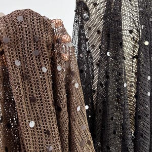 May include: Close-up of two pieces of open-weave fabric. One is a dark brown color, and the other is black. Both fabrics are embellished with round, shiny sequins. The fabrics are draped, creating folds and shadows.
