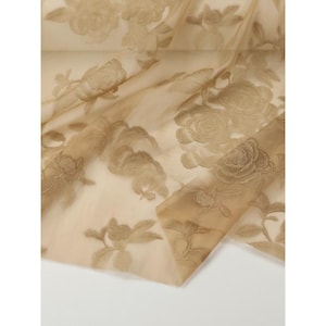 May include: A sheer, light beige fabric featuring an embroidered floral pattern in a matching tan thread. The design consists of detailed roses and leaves scattered across the translucent, lightweight material, creating a layered, textured appearance.