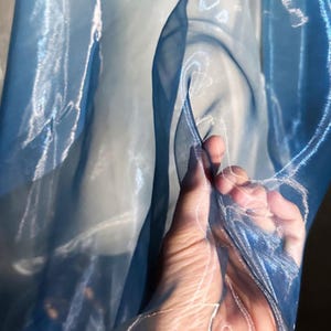 May include: A sheer, lightweight fabric in a gradient of blue tones, ranging from a deep, saturated navy to a pale, translucent sky blue. The material has a crisp, semi-transparent texture with visible folds and ripples that catch the light.