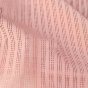 May include: Close-up of a light pink fabric with a vertical striped pattern. The fabric has a textured, semi-sheer appearance with a grid-like design within the stripes. The material is slightly wrinkled, adding depth to the image.
