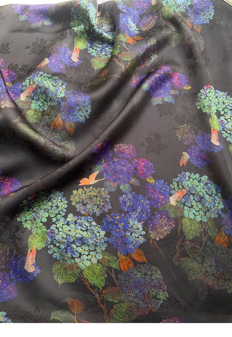 May include: Dark fabric with a floral pattern featuring blue, purple, and green hydrangea blooms. The fabric has a subtle sheen and a dark background, with hints of orange butterflies.