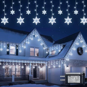 May include: A house decorated with white snowflake-shaped Christmas lights. The lights are strung along the roofline and hang down in a curtain-like fashion. The house has a white exterior and a dark blue night sky background.