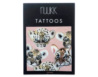 Può includere: Un set di tatuaggi temporanei con quattro adorabili volti di animali. I tatuaggi presentano una tigre, un leopardo e due cuccioli di ghepardo. I tatuaggi sono stampati su uno sfondo rosa con il testo "nuukk tattoos" in alto.