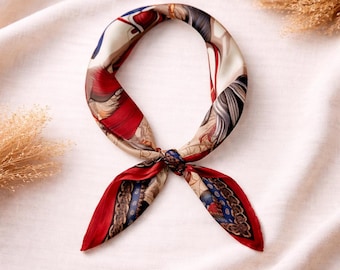 May include: A silk scarf with a detailed pattern featuring red, blue, and beige tones. The scarf is knotted at the center, with the ends spread out. The design includes figures and ornate borders.