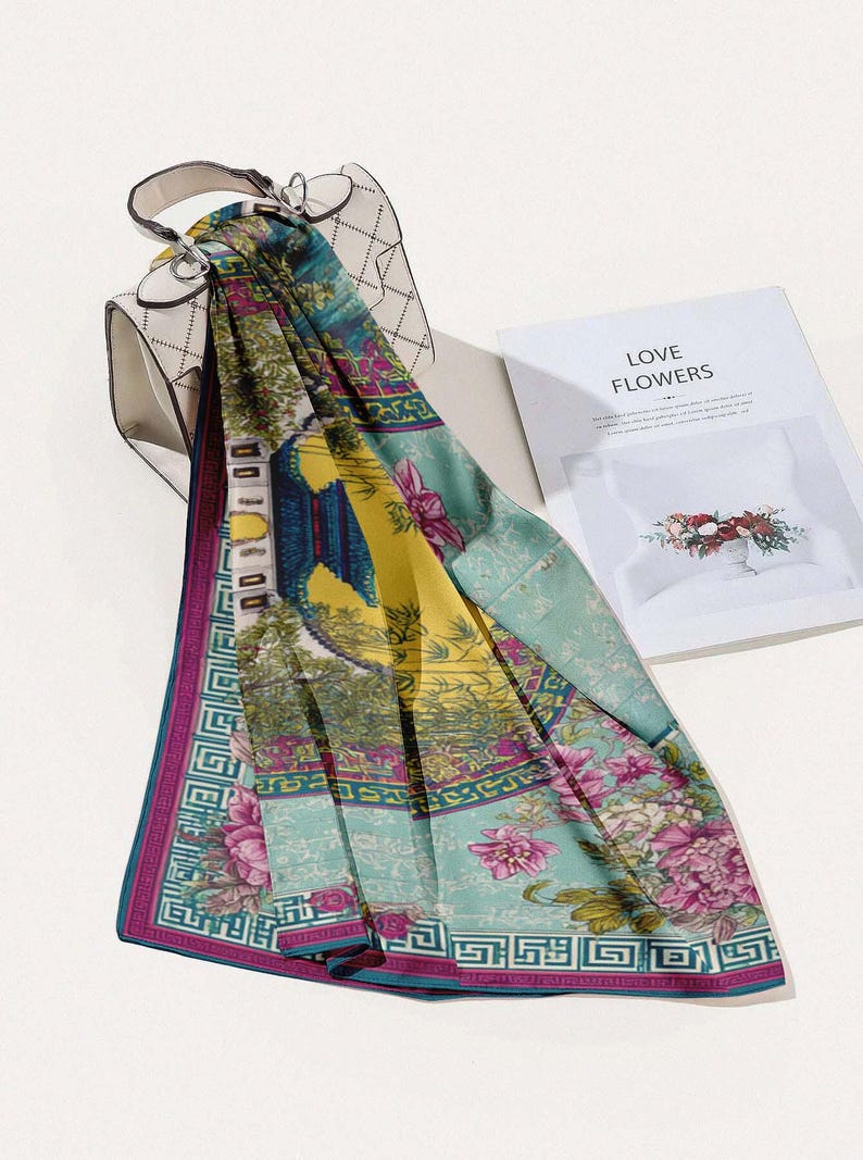 May include: A colorful scarf with a floral and architectural design, draped over a white handbag. The scarf features shades of teal, yellow, and pink with a geometric border. A book with the words "LOVE FLOWERS" is in the background.