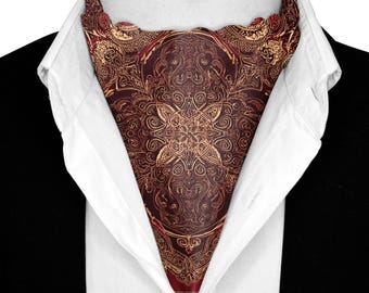 May include: A burgundy ascot with an ornate gold pattern is displayed against a white collared shirt and black suit jacket. The ascot features a symmetrical design with swirling details and a scalloped edge.