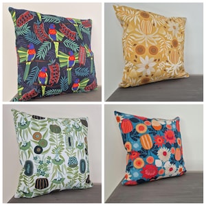 May include: A set of four square scatter cushions featuring distinct botanical and bird patterns. One cushion has a dark background with colourful parrots and red flowers, another is yellow with white flowers, one is white with green foliage, and one is blue with red flowers.