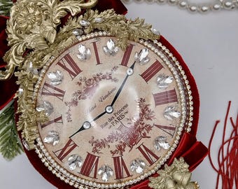 May include: An ornate clock with a burgundy velvet frame and accents. The clock face has Roman numerals, crystal embellishments, and the text "Rue des Princess PARIS". Gold filigree and a red velvet bow enhance the design.