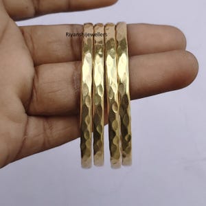 Könnte beinhalten: Vier goldfarbene Armreifen mit gehämmerten Strukturen. Die Armreifen sind gestapelt, und die Oberfläche hat ein gekerbtes Muster. Der Schmuck wird vor einem neutralen Hintergrund präsentiert. Der Text "Riyanshijewellers" ist sichtbar.