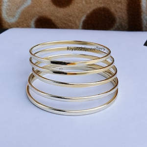May include: A stack of five thin, smooth, polished silver-tone bangles arranged in a conical formation. The metal bands have a reflective surface and a minimalist circular design. The text Riyanshijewellers is visible, and the stamp 925 is present.