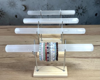Könnte beinhalten: Ein mehrstufiger Schmuckständer mit vier horizontalen weißen Selenitstäben, die von Metallarmen auf hellen Holzsockeln gehalten werden. Eine Sammlung von mehrfarbigen Edelsteinarmbändern ist auf dem vordersten Selenitstab angeordnet.