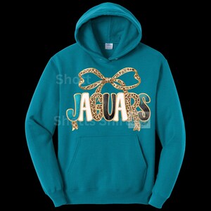 May include: Teal hooded sweatshirt with the word "JAGUARS" in a white, black, and leopard print design. A leopard print bow is above the word. The sweatshirt has a front pocket and a drawstring hood.
