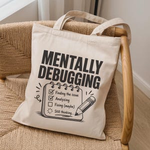May include: A cream-colored canvas tote bag featuring the black text MENTALLY DEBUGGING above a graphic of a spiral-bound notepad. The notepad shows a checklist with the items Finding the issue, Analyzing, Fixing (maybe), and Still thinking.