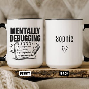 May include: A white ceramic mug with a black handle and rim. The front features the text MENTALLY DEBUGGING above a checklist with a pencil. The back displays the name Sophie above a small heart symbol. The design is printed in black ink.