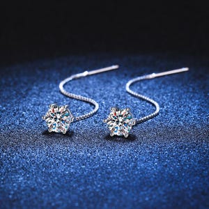 May include: A pair of silver threader earrings. Each earring features a sparkling, round-cut, clear gemstone set in a six-prong setting. The gemstones are connected to a delicate chain that extends into a straight post.