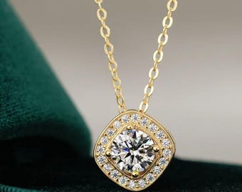 Può includere: Una collana color oro con un pendente quadrato. Il pendente presenta una grande gemma rotonda e trasparente circondata da gemme più piccole e trasparenti. La catena della collana è anch'essa dorata e delicata. Lo sfondo è verde scuro.