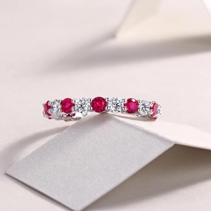 Peut inclure: Une bague en argent ornée de pierres précieuses rouges et claires alternées. Le design de la bague est mis en valeur sur un fond neutre. Les pierres sont taillées en rond. Un bijou classique, adapté à toutes les occasions.