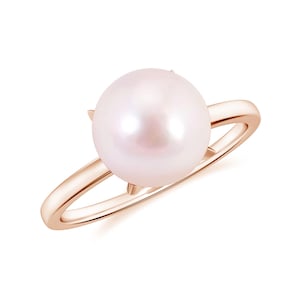 Könnte beinhalten: Ein roségoldener Ring mit einer großen, runden Perle. Die Perle hat einen zarten rosa Farbton, und der Ring hat ein schlichtes, elegantes Design. Die Perle wird von vier filigranen Krappen gehalten.
