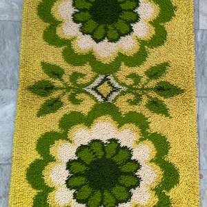 May include: A rectangular, shag-style rug with a floral pattern. The rug features large, stylized flowers in shades of green, cream, and yellow. The background is a solid yellow, and the rug has a textured, plush appearance.