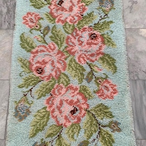 May include: A rectangular, light blue rug with a floral design. The rug features pink roses, green leaves, and small blue flower clusters. The rug is approximately 36 inches long and 18 inches wide.