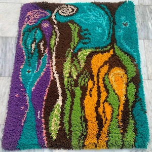 May include: A rectangular, shaggy rug with an abstract design. The rug features a vibrant color palette including teal, purple, brown, green, and orange. The design has a textured, raised appearance, creating a tactile and visually interesting piece.