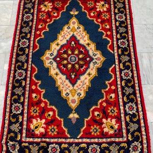 May include: A rectangular area rug featuring a central diamond medallion in red, cream, and navy blue. The rug has a deep navy blue field surrounded by a wide red border, with intricate floral and geometric patterns in gold, white, and blue.