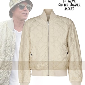 Puede incluir: Chaqueta bomber acolchada de color crema con un patrón de diamantes, cremallera frontal y puños y dobladillo acanalados. La chaqueta tiene cuello alzado y dos bolsillos con cierre de botón a presión. Texto: "BRAD PITT F1 MOVIE QUILTED BOMBER JACKET."