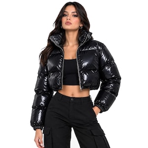 May include: A cropped puffer jacket in a glossy black finish featuring a high collar, horizontal quilted channels, and a full-length silver-toned front zip. The jacket has long sleeves with elasticated cuffs and a boxy, waist-length silhouette.