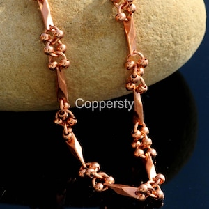 May include: A copper-colored necklace with a unique design. The necklace features diamond-shaped links and clusters of small, round beads. The word "Coppersty" is printed on the image.