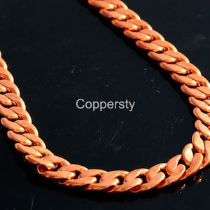 Puede incluir: Un collar de cadena de color cobre. La cadena está hecha de eslabones entrelazados y se muestra sobre un fondo negro. El texto "Coppersty" es visible en la imagen.