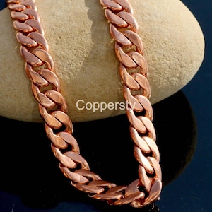 Puede incluir: Un collar de cadena de color cobre con un diseño de eslabones de bordillo. El collar se muestra sobre una piedra de color marrón claro sobre un fondo oscuro. La palabra "Coppersty" está impresa en la piedra. La cadena es de cobre.