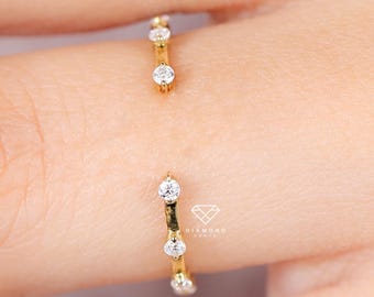 Puede incluir: Un anillo abierto de color dorado con tres pequeñas piedras preciosas transparentes engastadas a lo largo de la banda. El anillo se muestra en un dedo, con las piedras preciosas captando la luz. Una joya delicada.