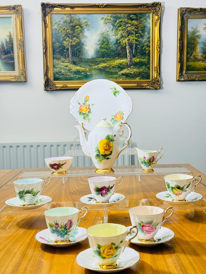 May include: A vintage tea set featuring a white teapot, creamer, sugar bowl, and several teacups and saucers. The set is decorated with yellow roses and gold trim. A white serving plate with rose accents is also included.
