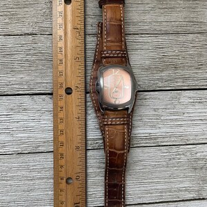 May include: A brown leather wristwatch with a silver case and a white face. The watch has a white stitching detail on the band.