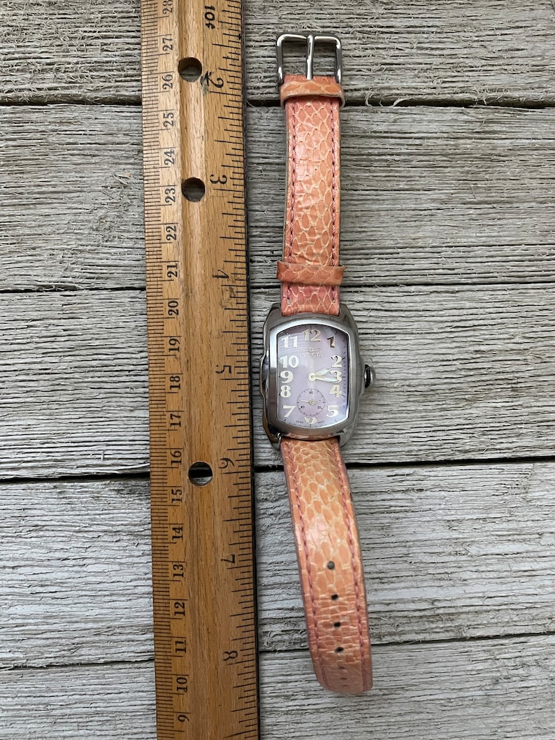 May include: A silver wristwatch with a pink leather band. The watch face is white with black Roman numeral hour markers and black hands. The watch is about 2 inches in diameter.