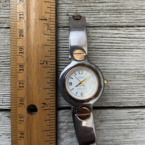 May include: A silver and gold tone wristwatch with a white face and black hands. The watch face has the text "ECCLISSI STERLING SILVER" on it.