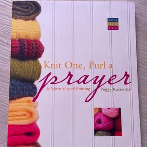 Op de afbeelding: Boekomslag met de titel "Knit One, Purl a prayer: A Spirituality of Knitting" door Peggy Rosenthal. De omslag toont een stapel kleurrijke gebreide stoffen en een close-up van garenbollen.
