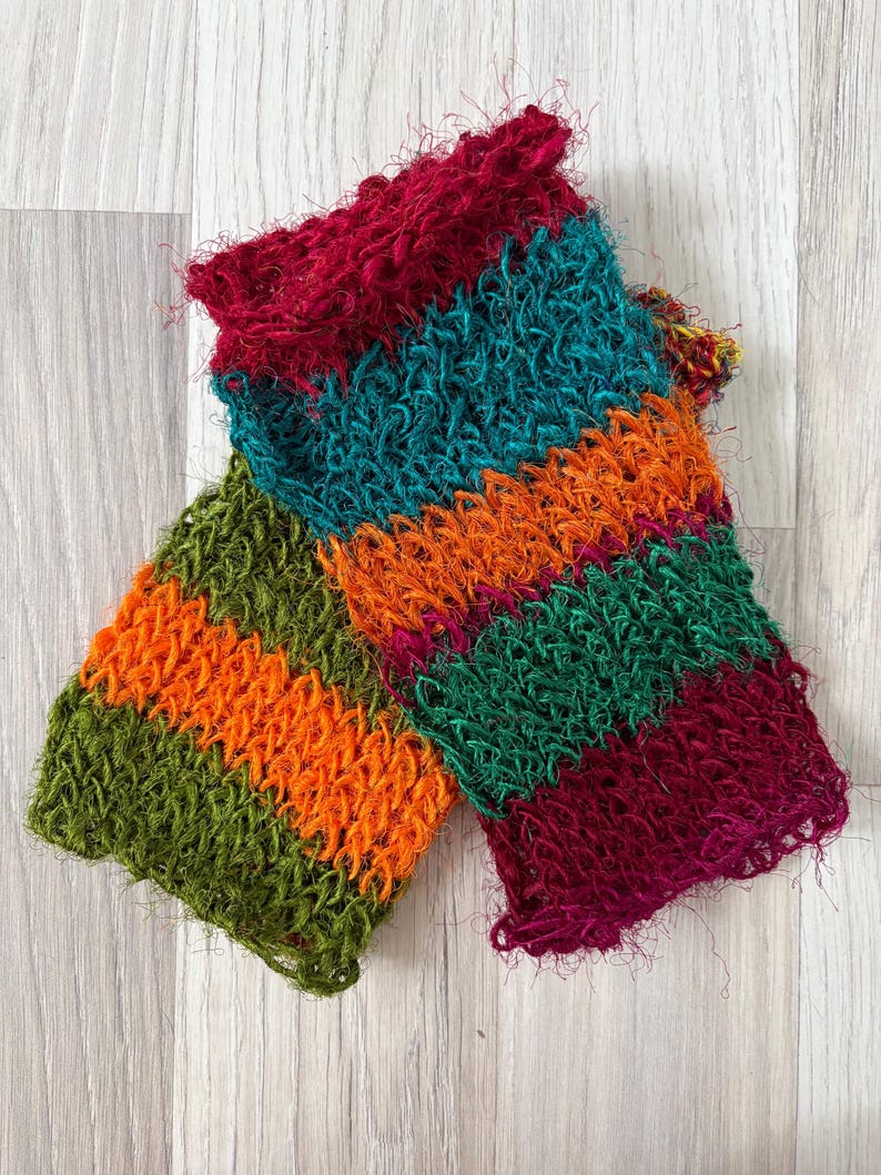 May include: A pair of fingerless gloves featuring a textured, open-knit construction with horizontal stripes in vibrant shades of deep red, teal, bright orange, forest green, and magenta. The yarn has a fuzzy, slightly frayed appearance.