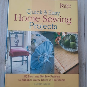 May include: A book titled "Quick & Easy Home Sewing Projects" by Reader's Digest with a yellow cover and a photo of a chair, a pillow, and a table setting. The book features 50 low- and no-sew projects to enhance every room in your home by Gloria Nicol.