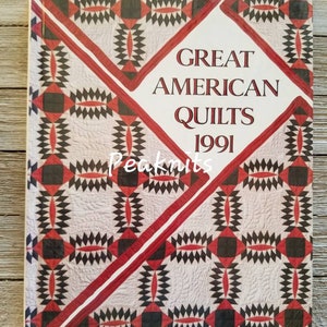 Op de afbeelding: Een boek getiteld "Great American Quilts 1991" met een rood, zwart en wit quiltpatroon op de omslag.