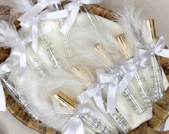 May include: A woven basket filled with small glass perfume bottles. Each bottle is adorned with a white ribbon and a pearl. The bottles are nestled in white feathers. Some bottles have silver caps, others gold.
