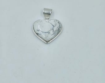 May include: A heart-shaped pendant with a silver-colored bail. The pendant features a white stone with gray veining, set in a silver-colored frame. The pendant is displayed against a white background.