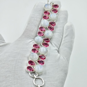 Peut inclure: Un bracelet en argent composé d'une rangée centrale de pierres de lune rondes et translucides alternant avec des pierres roses facettées en forme de poire. Le design comprend une extension de chaîne en métal avec des maillons circulaires.