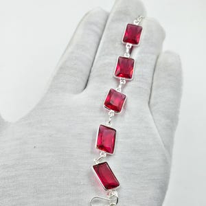 May include: A silver bracelet with five rectangular, bright red gemstones. Each gemstone is set in a silver frame and linked together. The bracelet is fastened with a silver clasp. The gemstones are a vivid shade of red.