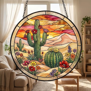 May include: Round stained glass window featuring a desert scene with cacti and colorful flowers. The artwork has a black metal frame and is suspended by a chain. The background depicts a sunset with warm orange, yellow, and red hues.