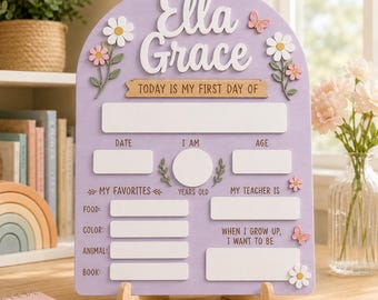 Peut inclure: Un panneau de suivi en bois en forme d'arche violet clair avec le nom Ella Grace en lettres blanches en relief. Il comporte des espaces blancs pour noter la date, l'âge, les favoris et les objectifs, décoré de marguerites et de papillons.