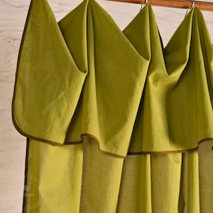 May include: Olive green curtains with a brown trim are suspended from a wooden rod. The fabric is folded in a decorative pattern. The word "NISHH" is visible on the left side of the image.