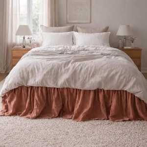 May include: A bedroom with a bed dressed in white linen and a rust-coloured bed skirt. Two wooden bedside tables with lamps sit either side of the bed. A woven pendant light hangs above, and a neutral rug covers the floor.