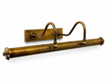 May include: A vintage-style brass picture light fixture. The fixture has a rectangular backplate with curved arms and a cylindrical light bar. The ends of the light bar have decorative starburst designs. The fixture is mounted on a white wall.